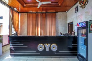A reception desk with the name "OYO" prominently displayed, a ceiling fan, and a refrigerator stocked with beverages. - Super OYO 1952 Hotel Dewata Indah (Denpasar)