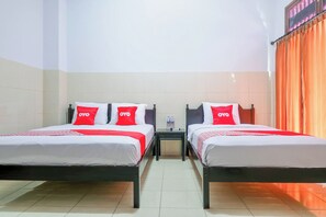 A hotel room with two beds, each with white bedding and red pillows, a small table between the beds, and an orange curtain on the right side. - Super OYO 1952 Hotel Dewata Indah (Denpasar)