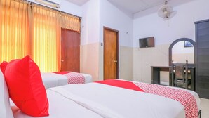 Ein Hotelzimmer mit zwei Betten, einem Schreibtisch, einem Sessel, einer Klimaanlage und einem Fernseher.