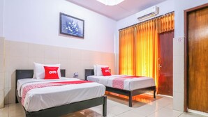 Habitación de hotel con dos camas, cada una con ropa blanca de cama y almohadas rojas, un cuadro floral enmarcado en la pared y un equipo de aire acondicionado sobre la cama.
