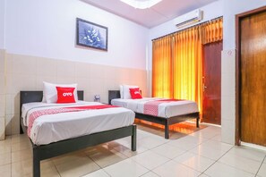 Habitación de hotel con dos camas, cada una con ropa blanca de cama y almohadas rojas, un cuadro floral enmarcado en la pared y un equipo de aire acondicionado sobre la cama.
