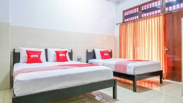 A hotel room with two beds, each with white bedding and red pillows, and a large window with orange curtains.
