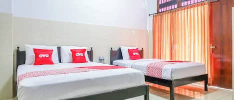 Habitación de hotel con dos camas, cada una con ropa blanca y almohadas rojas, y un ventanal con cortinas naranjas.