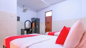 Une chambre d’hôtel avec deux lits, une armoire en bois, un miroir et un ventilateur de plafond.