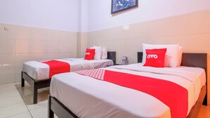 Ein Hotelzimmer mit zwei Betten, jeweils mit weißer Bettwäsche und roten Akzenten, darunter Kissen und eine Decke. Darüber hängt ein gerahmtes Bild an der Wand.