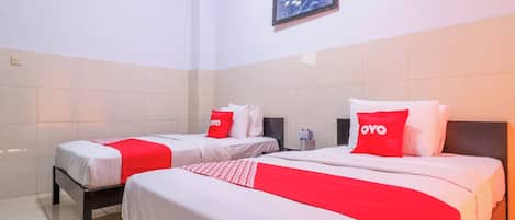 A hotel room with two beds, each with white bedding and red accents, including pillows and a blanket. There is a framed picture on the wall above the beds.
