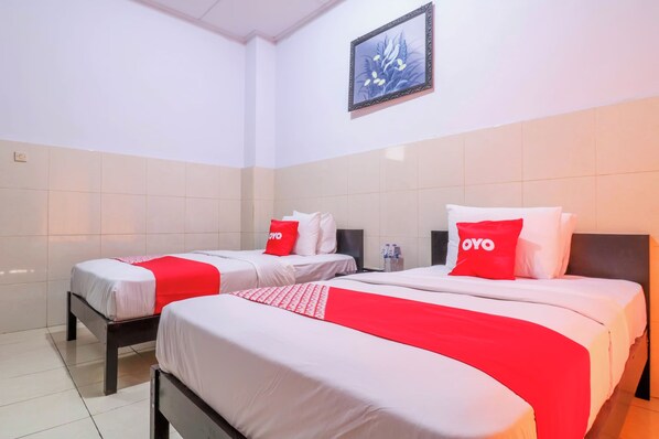 A hotel room with two beds, each with white bedding and red accents, including pillows and a blanket. There is a framed picture on the wall above the beds. - Super OYO 1952 Hotel Dewata Indah (Denpasar)