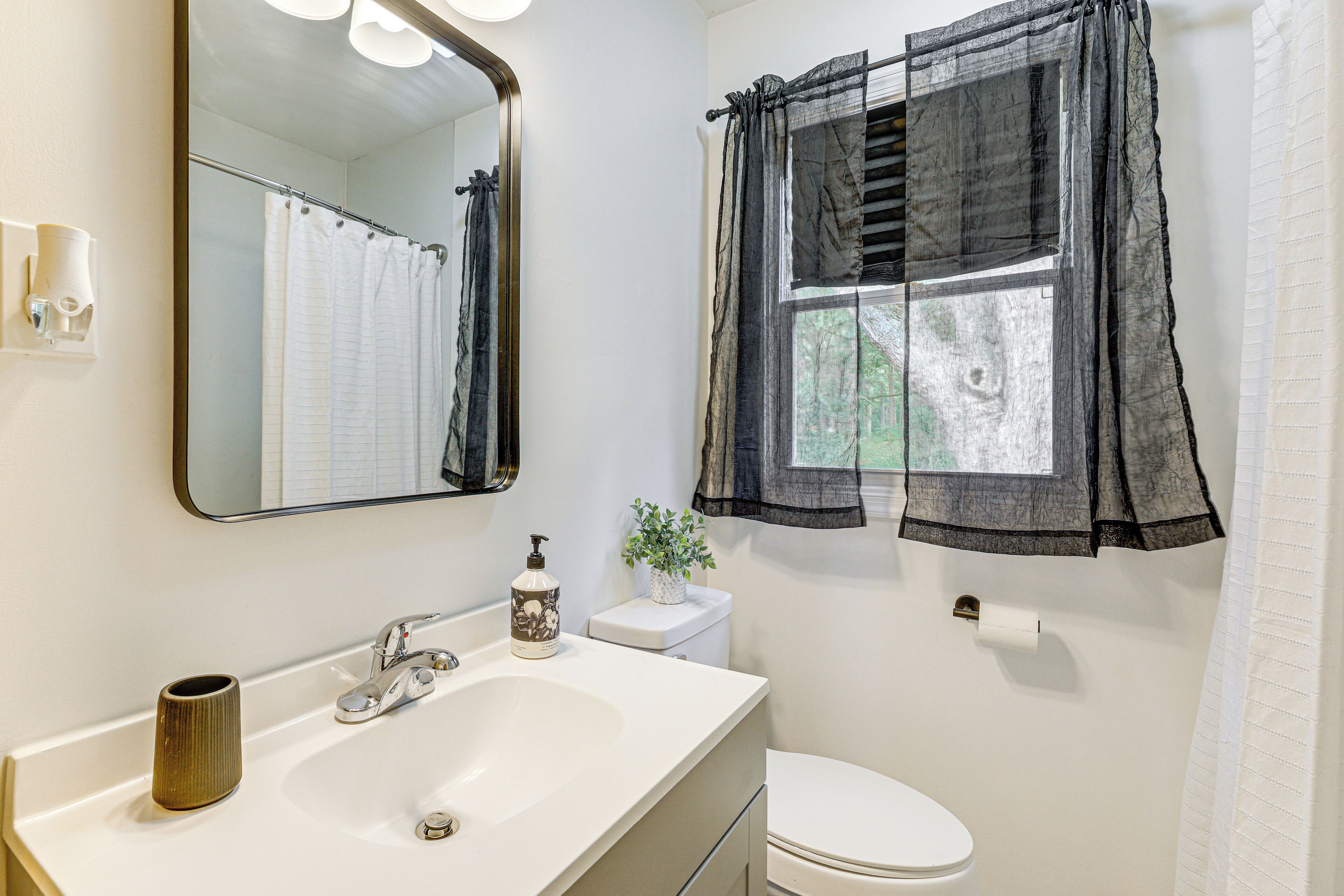 A bathroom with a white sink, a mirror, a toilet, and a window with a black curtain.