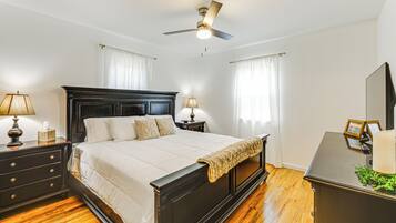 A bedroom with a large bed, wooden floor, ceiling fan, bedside lamps, and a dresser.