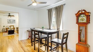 Un coin repas avec une table et des chaises en bois, un ventilateur de plafond et une grande horloge murale.