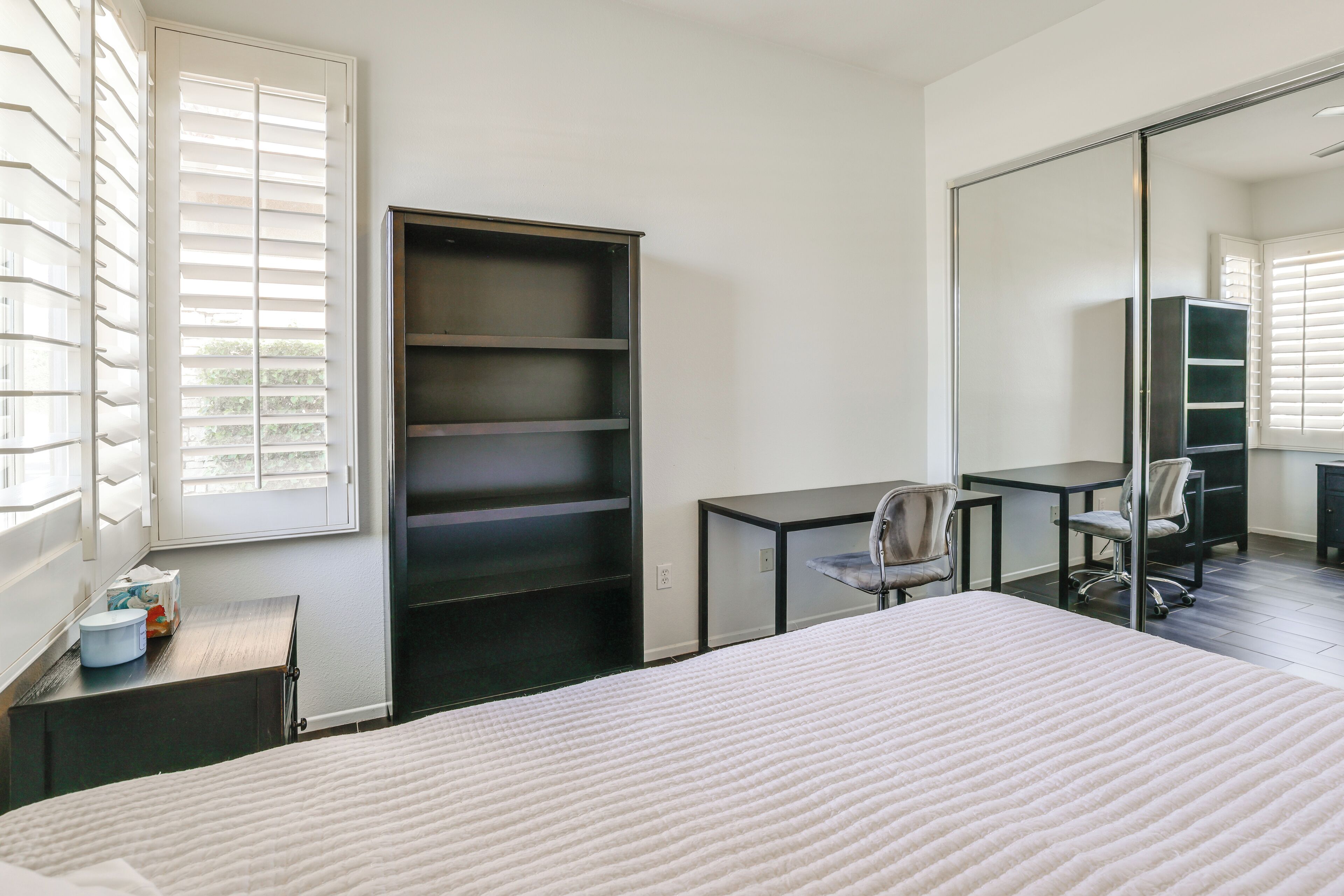 A bedroom with a bed, a desk, a chair, a wardrobe, and a large mirror.