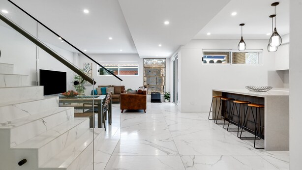 A modern kitchen with a marble countertop, a dining area with a sofa and a TV, and a staircase leading to another level. - Spacious Lidcombe Lux mins to Sydney Olympic Park (Lidcombe)