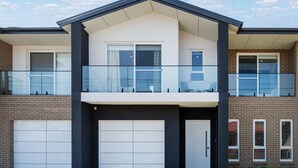 A two-story residential building with a balcony, large garage doors, and a brick facade. - Spacious Lidcombe Lux mins to Sydney Olympic Park (Lidcombe)