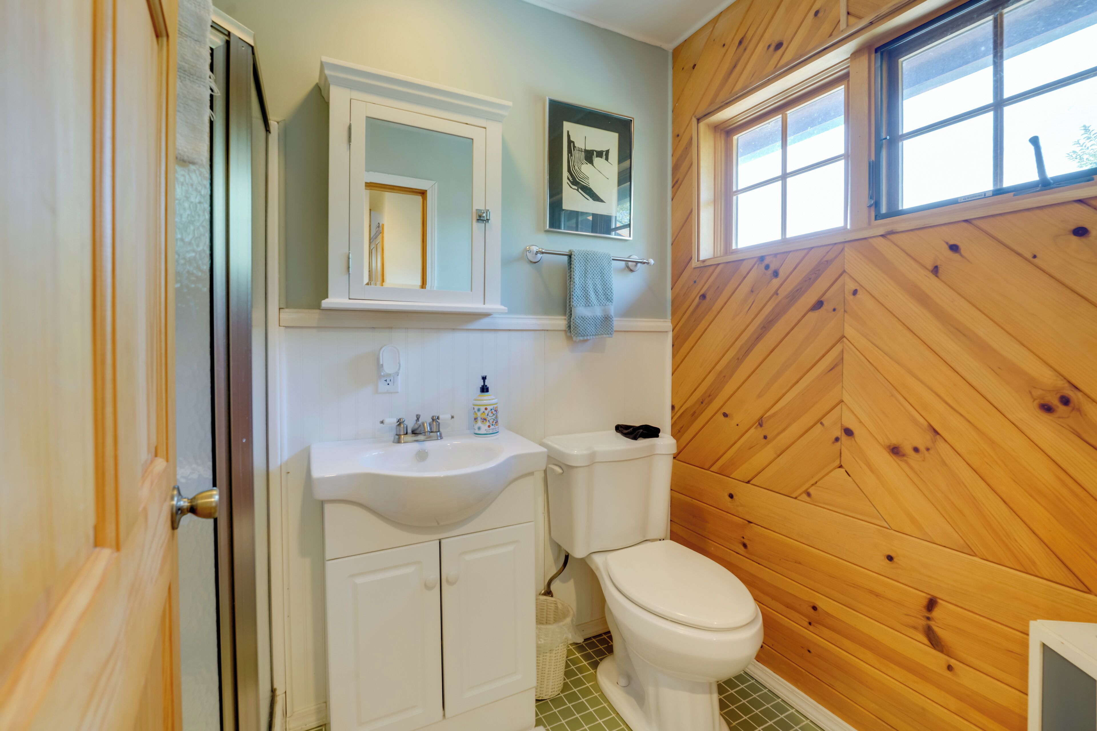A bathroom with a wooden wall, a white sink, a mirror, and a toilet.