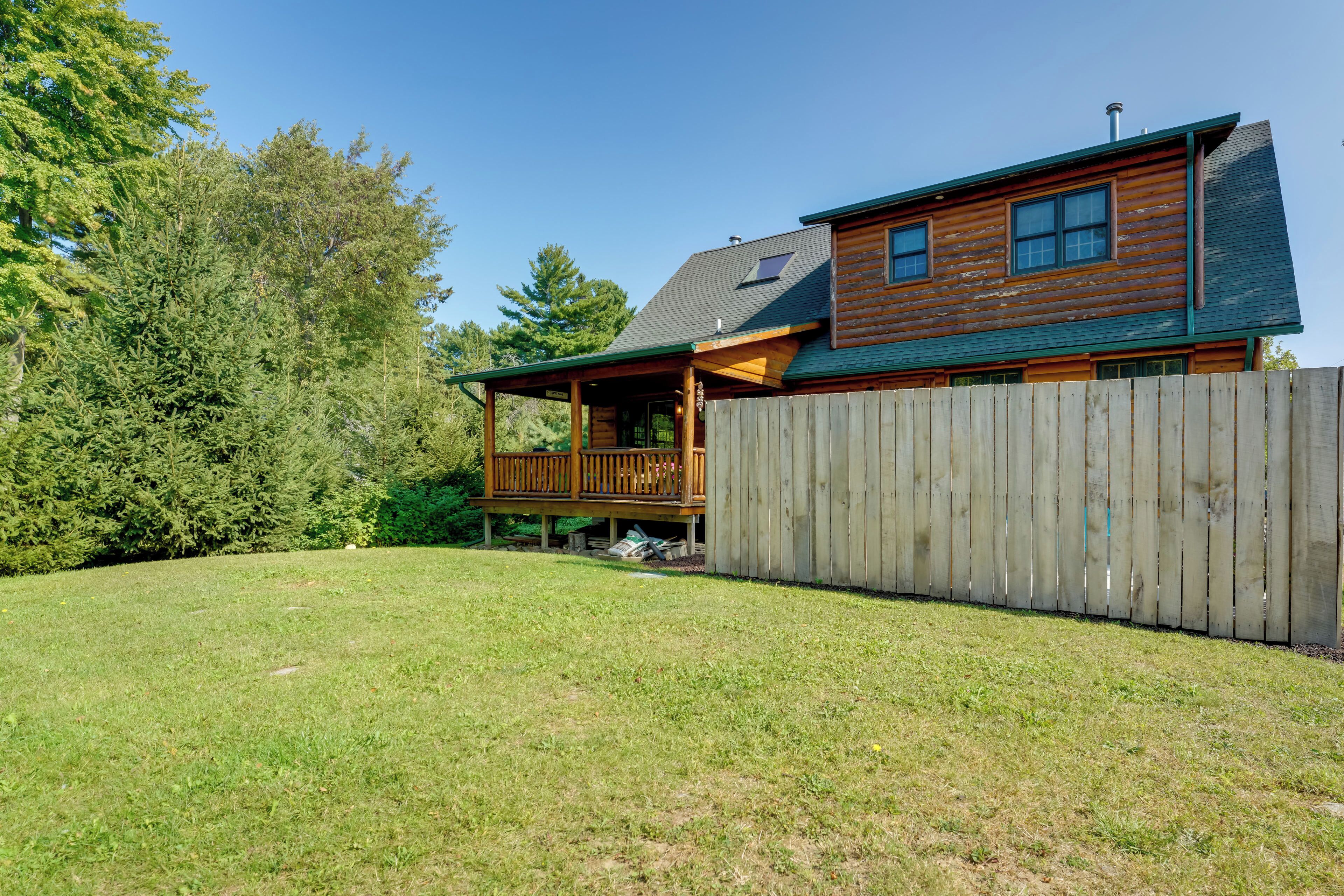 Una cabaña de madera con terraza, rodeada por una valla de madera y un patio cubierto de césped.