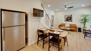 Ein modernes Wohnzimmer mit einer Couch, einem Esstisch mit Stühlen, einem an der Wand befestigten Flachbildfernseher und einem Deckenventilator.