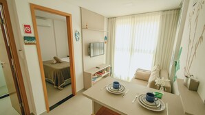 A compact hotel room with a bed, a small dining area with a table and chairs, a television, and a window with curtains. - Beach apartment on the Brazilian northeast coast - Maracaípe. (Ipojuca)