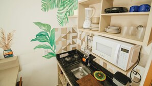 A compact kitchen with a microwave, stove, and shelves with dishes and cups. - Beach apartment on the Brazilian northeast coast - Maracaípe. (Ipojuca)