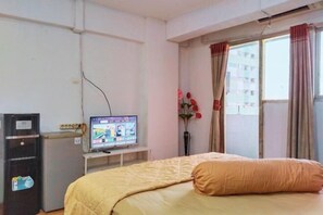 Une chambre d’hôtel avec un lit, un téléviseur posé sur un meuble, un bureau avec un ordinateur et une fenêtre avec des rideaux.