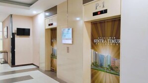 Een hotel lobby met een modern design, met een receptiebalie, liften en een grote poster die het hotel promoot.