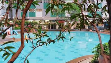 Piscina interior com chão revestido, rodeada por vegetação e um edifício ao fundo.