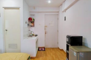 A small, compact room with a bed, a kitchenette, a refrigerator, and a door leading to another room.
