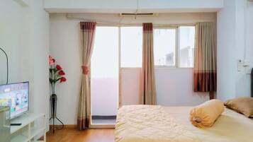 Quarto com cama, cortinas, televisão e um vaso de flores.