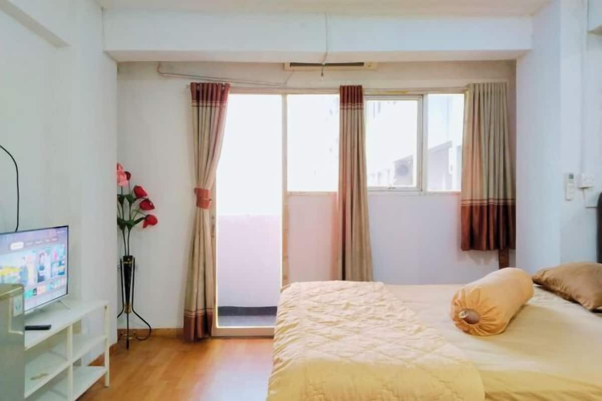 Une chambre à coucher avec un lit, des rideaux, une télévision et un vase rempli de fleurs.
