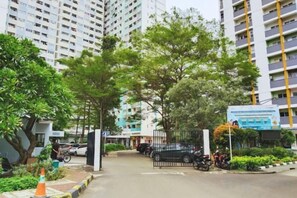 A gated residential complex with high-rise buildings, trees, and parked vehicles.