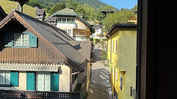 Blick aus einem Fenster auf eine enge Straße mit traditioneller Bebauung, im Hintergrund ein Berg und ein klarer Himmel.