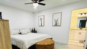Une chambre à coucher avec un lit, un ventilateur de plafond et un petit pouf.
