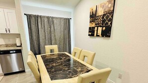 Un coin repas avec une table en marbre et quatre chaises, une cuisine équipée d’un lave-vaisselle, et une œuvre d’art représentant un paysage urbain accrochée au mur.