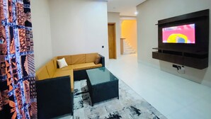 Ein modernes Wohnzimmer mit einer Eckcouch, einem Glastisch und einem flachbildfernseher an der Wand.