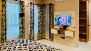 Ein modernes Schlafzimmer mit Bett, Fernseher, Klimaanlage und einem Regal mit einer Kaffeemaschine.
