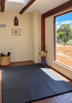A room with a large window, a mat on the floor, a wall-mounted light, and a framed picture.