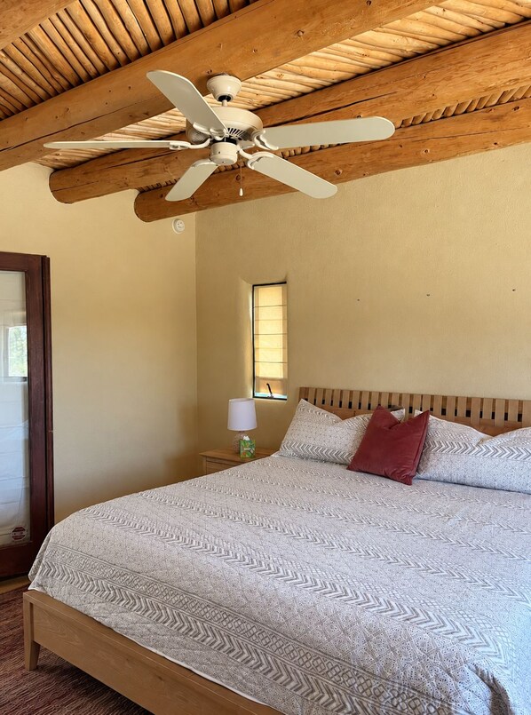 A bedroom with a wooden ceiling, a bed with patterned bedding, a nightstand with a lamp, and a window.