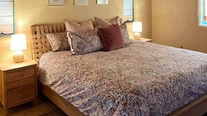 A bedroom with a wooden ceiling, a bed with patterned bedding, two bedside tables with lamps, and framed pictures on the wall. - Charming 3-bedroom/3 full bath home in lovely Santa Fe, private and peaceful (Santa Fe)