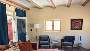A living room with a red sofa, a round ottoman, a lamp, two chairs, a cactus, and a framed picture on the wall. - Charming 3-bedroom/3 full bath home in lovely Santa Fe, private and peaceful (Santa Fe)