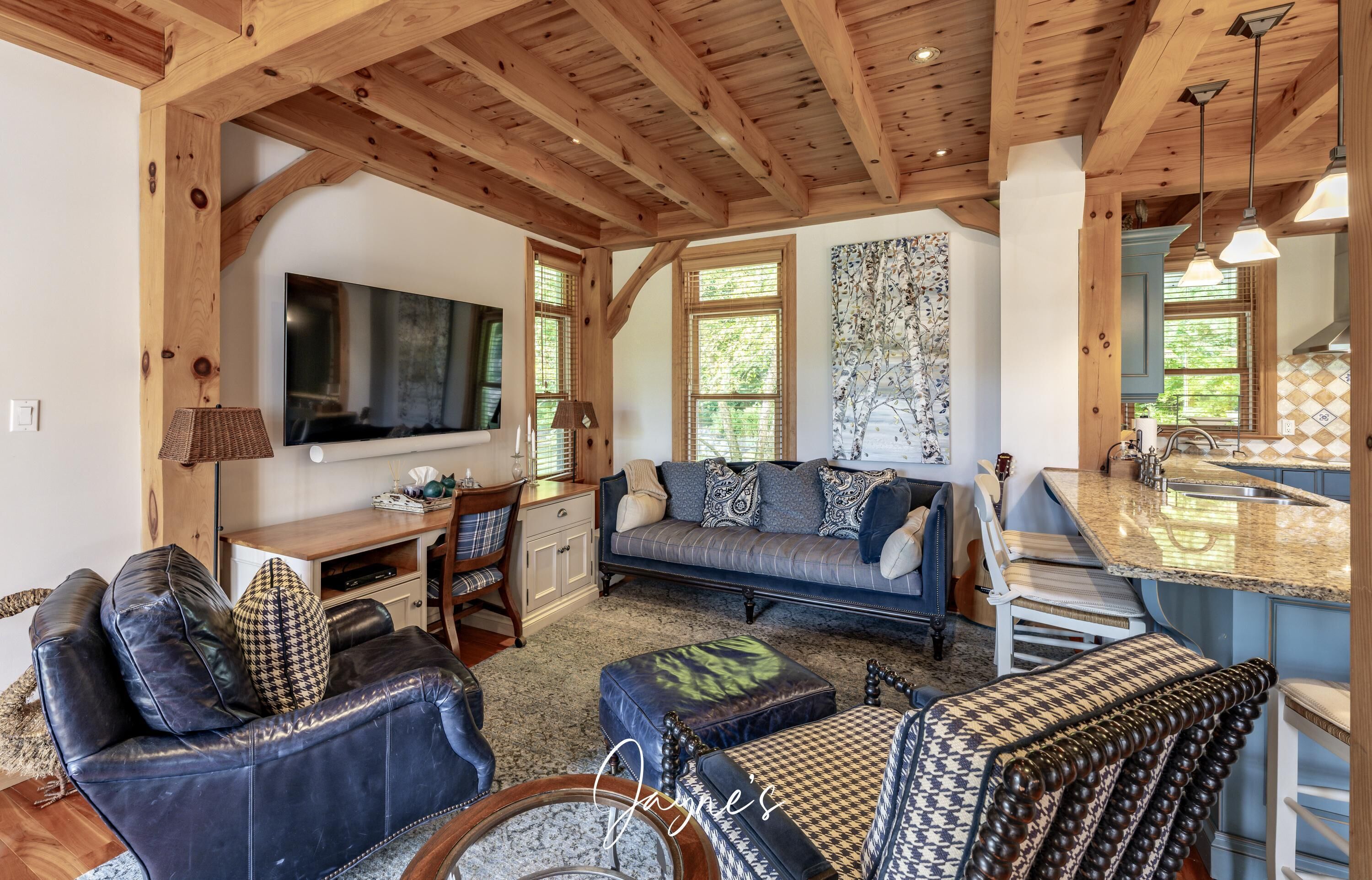 A cozy living room with a sofa, chairs, and a TV. There's a kitchen area with a counter and sink.