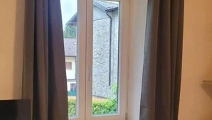 Una stanza con finestra, tende, termosifone e pavimento piastrellato.