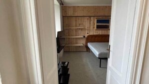 Un corridoio stretto che conduce a una stanza con un letto, pannelli di legno e una finestra.