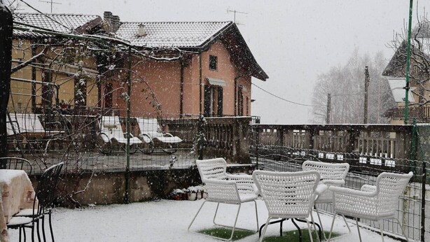 Un'area salotto esterna innevata con sedie, tavoli, una recinzione e un edificio con tetto in tegole.