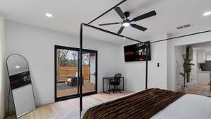 Une chambre moderne dotée d’un grand lit, d’un ventilateur de plafond, d’un téléviseur fixé au mur et d’une porte-fenêtre coulissante donnant sur un espace extérieur.