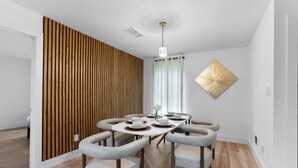 Un espace repas moderne avec une table ronde, six chaises et un mur décoratif en bois.