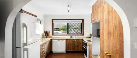 A compact kitchen with white appliances, wooden cabinets, and a window with a view.