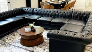 A living room with a sectional sofa, a round coffee table, and a dining area with chairs and a table.