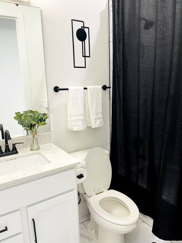 Un baño con inodoro blanco, toallero negro y cortina de ducha negra.