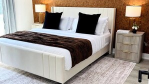 A bedroom with a large bed, two bedside tables, a patterned rug, and a wooden floor.