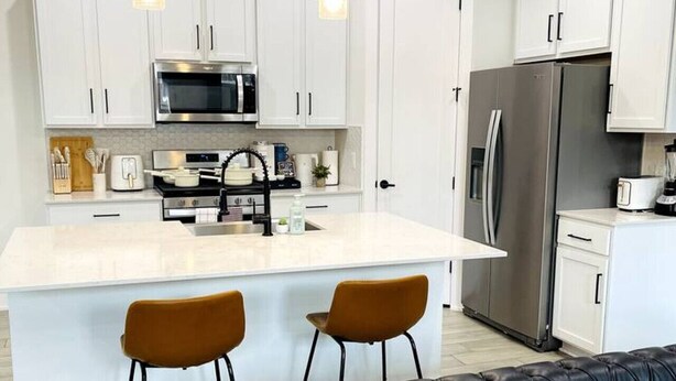 A modern kitchen with white cabinets, a stainless steel refrigerator, and a central island with two stools.