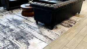 A living room with a sectional sofa, a coffee table, and a rug. There is a dining table with chairs in the background.